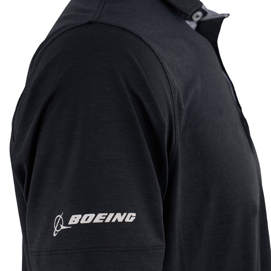 A close-up of someone wearing the Boeing T-7A Red Hawk Series Men’s Polo by BOEING, featuring a black design, white logo and name on the left sleeve, buttoned placket, moisture-wicking fabric, and a plain white background.