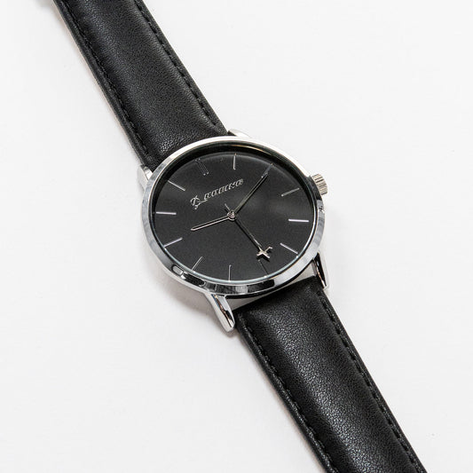 The Boeing Silver Rotating Airplane Watch by Boeing features a minimalist black dial encased in a silver case with a sleek black leather strap. Silver hour markers and hands move elegantly, showcasing timeless style as it rests gracefully on a white surface.