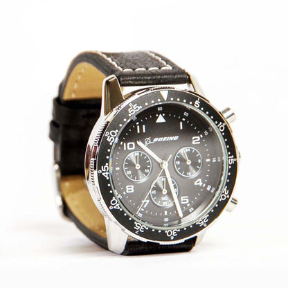 The Boeing Stores Boeing Black Leather Watch is a mens analog wristwatch boasting a Japanese movement, a stainless steel case with a black dial, three subdials, white markings including the number 60 at the top, and a tachymetric bezel for precision.