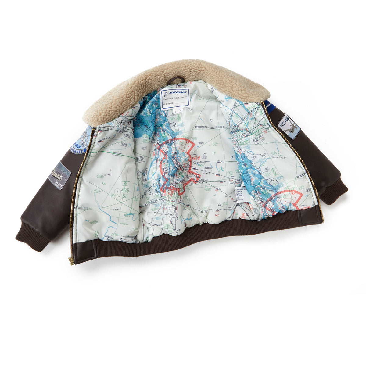The Boeing Stores Boeing Kids Brown Aviator Jacket features a shearling-fleece collar, a vintage-style map lining with red markings, and aviation-themed patches and badges on the sleeves.