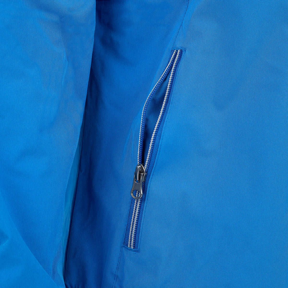 Close-up of a blue Boeing Newport Womens Jacket by The Boeing Store showing a partially open zippered pocket. It features a smooth, slightly shiny fabric with breathable TPU membrane, and the silver zipper has a small pull tab.
