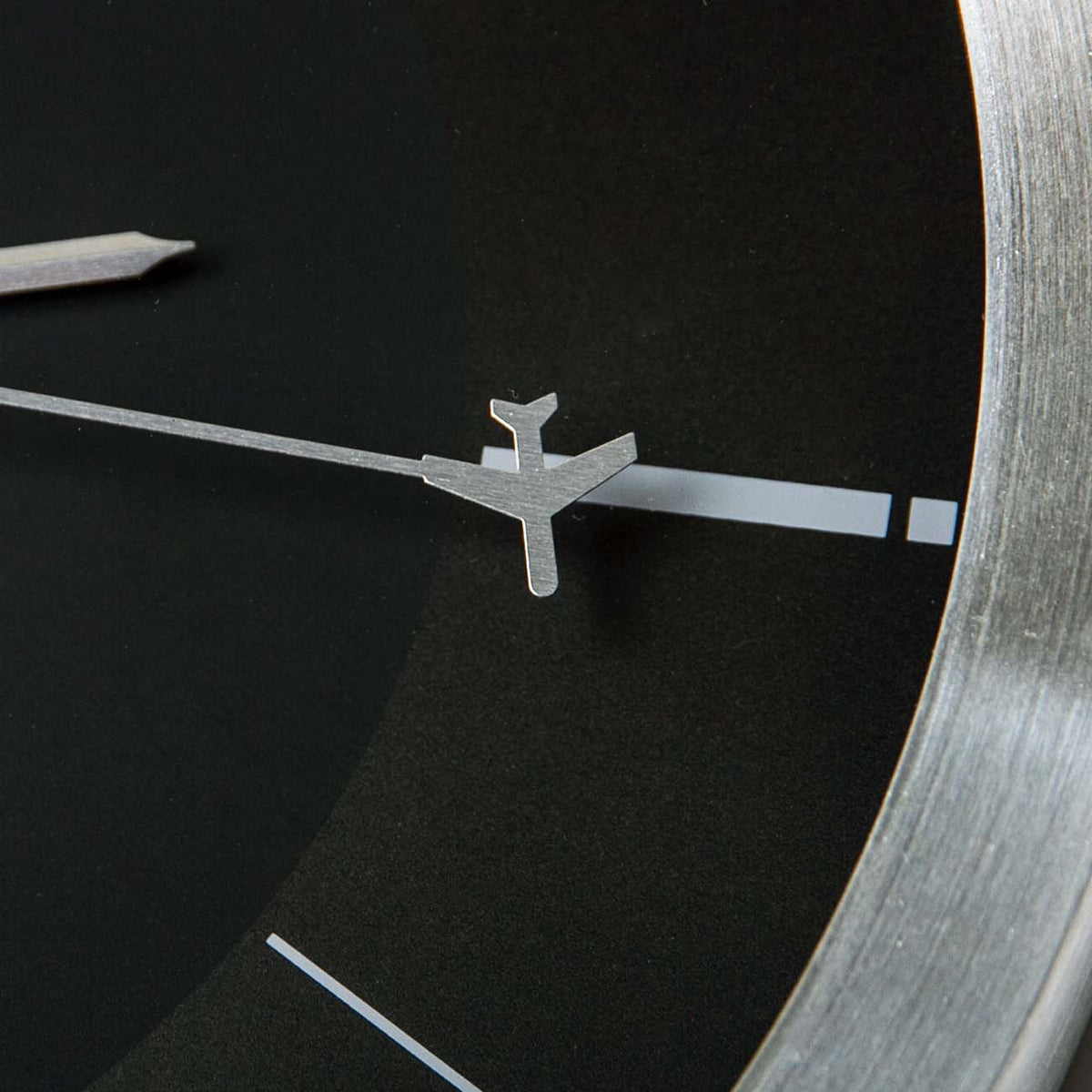 Close-up of the Boeing Rotating Plane Clock by The Boeing Store, a minimalist design featuring a black face, simple white hour markers, and a unique silver airplane-shaped second hand.