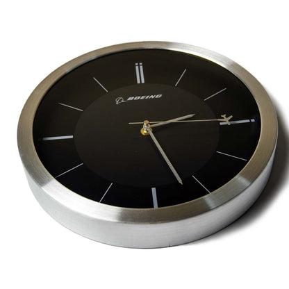 The Boeing Rotating Plane Clock by The Boeing Store features a black face, silver frame, minimalist white markers, and the Boeing logo at the top. Inspired by airplane design, its hands show the time as about 10:10.