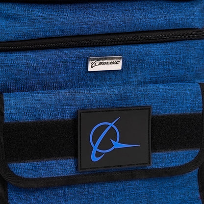 The Boeing Double Deck Lunch Box, from The Boeing Store, is a blue fabric bag featuring a metal Boeing plaque on top and a larger blue logo with a stylized plane on a black patch. It has a black horizontal strip in the middle and comes with a removable shoulder strap for easy carrying.