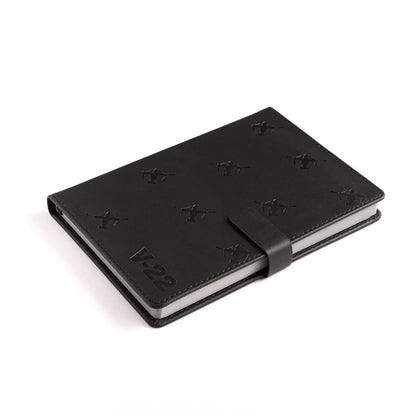 The Boeing Stores Boeing V-22 Osprey Notebook features a black PU hardcover, magnetic strap closure, embossed X shapes, and V-22 text in the bottom left corner, displayed on a white background.