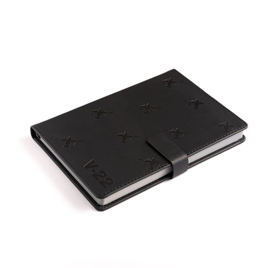 The Boeing Stores Boeing V-22 Osprey Notebook features a black PU hardcover, magnetic strap closure, embossed X shapes, and V-22 text in the bottom left corner, displayed on a white background.