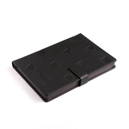 A Boeing CST-100 Starliner Notebook from The Boeing Store, featuring a black PU hardcover with raised geometric patterns and a matching strap closure, lies on a white surface. Its sleek design, resembling an aircraft stamp, includes subtle embossed details symbolizing Boeings precision.
