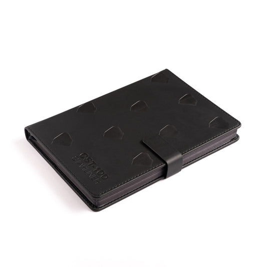 A Boeing CST-100 Starliner Notebook from The Boeing Store, featuring a black PU hardcover with raised geometric patterns and a matching strap closure, lies on a white surface. Its sleek design, resembling an aircraft stamp, includes subtle embossed details symbolizing Boeings precision.