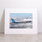 Showcased on a light surface against a plain white background, the Boeing 777-9 Matted Print - Small by Boeing features a high-resolution image of a Boeing 777 airplane soaring above the clouds. This elegant matted print delivers exceptional clarity through digital printing and proudly displays the iconic Boeing logo.