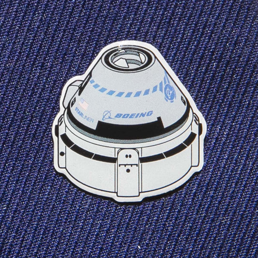 A Boeing Illustrated Starliner Lapel Pin by The Boeing Store features a spacecraft design on blue fabric. It showcases an epoxy finish and small logos, including the Boeing logo, for a realistic touch.