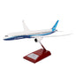 The Boeing Unified 787-10 Dreamliner 1:200 Model by The Boeing Store is displayed on a wooden stand, featuring its sleek white and blue design with a visible engine and unique wing shape. This model embodies the elegance and innovation of the renowned 787 family.