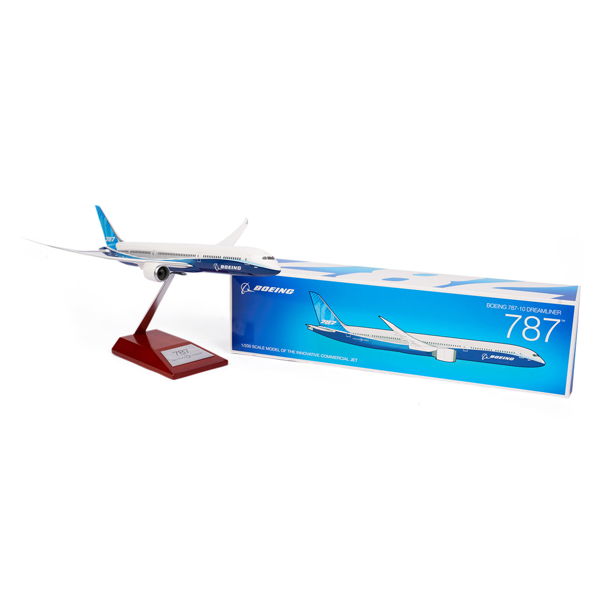 A 1:200 Boeing Unified 787-10 Dreamliner model by The Boeing Store is on a wooden stand. The white model with blue accents is displayed alongside a blue and white box featuring the aircraft image and Boeing logo, celebrating the 787 family.