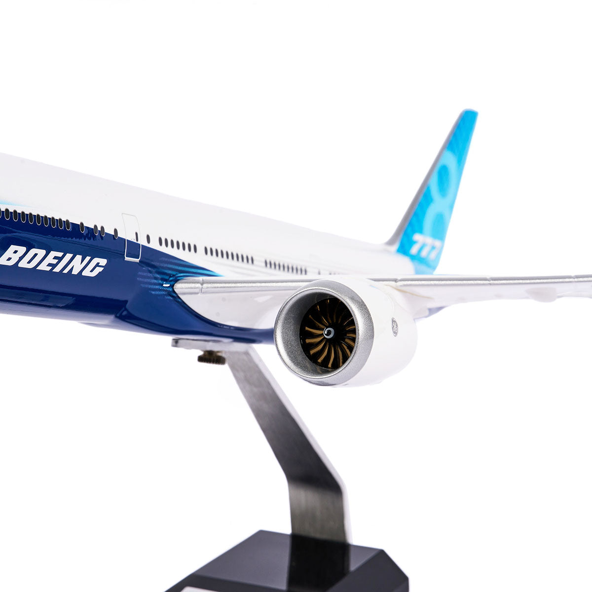 Close-up of the Boeing Unified 777-8 1:144 Model from The Boeing Store, featuring BOEING on the fuselage reminiscent of the Boeing 777X. It highlights twin-engine jet and wing details, elegantly mounted on a metal stand with a black base.