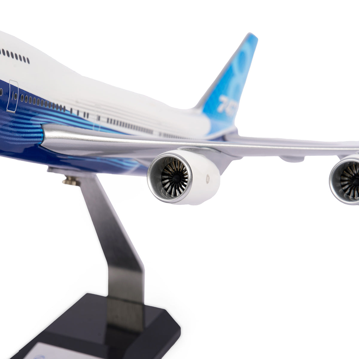 A close-up of The Boeing Store’s Boeing Unified 747-8i 1:144 Model on a stand, showcasing its detailed engines, wing, and tail in blue and white livery—emphasizing premium quality against a clean white background.