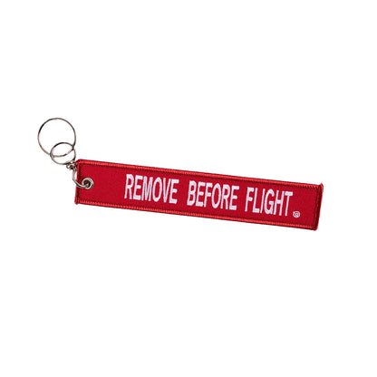 The Boeing T-7A Remove Before Flight Keychain, a red fabric tag with bold white REMOVE BEFORE FLIGHT lettering, includes a sturdy metal keyring. Ideal for aviation enthusiasts or frequent flyers.