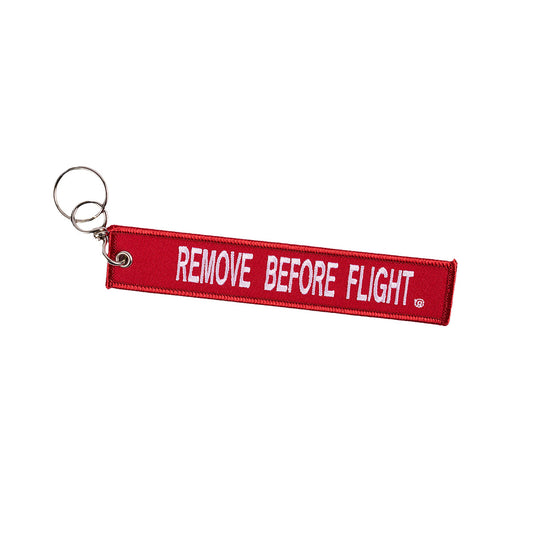 The Boeing T-7A Remove Before Flight Keychain, a red fabric tag with bold white REMOVE BEFORE FLIGHT lettering, includes a sturdy metal keyring. Ideal for aviation enthusiasts or frequent flyers.