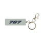 The BOEING 767 Series Keychain is a light gray, rectangular rubber accessory featuring "767" in bold, dark blue, embossed lettering. This aviation-themed keychain comes attached to a silver metal split ring and a lobster claw clasp, all showcased against a plain white background.