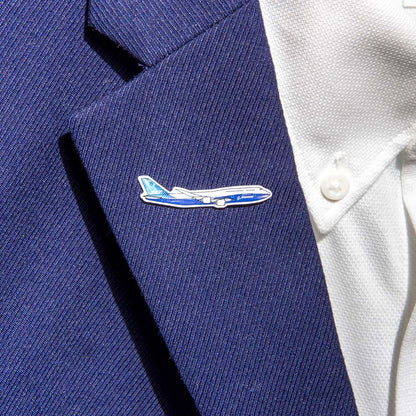 A person wears a blue suit jacket and white shirt, complemented by The Boeing Stores Boeing Illustrated 747 Lapel Pin—silver-toned and airplane-shaped with an epoxy finish in blue and white hues.