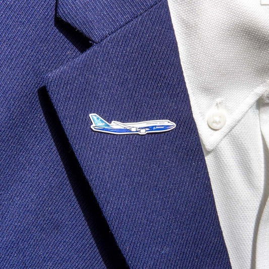 A person wears a blue suit jacket and white shirt, complemented by The Boeing Stores Boeing Illustrated 747 Lapel Pin—silver-toned and airplane-shaped with an epoxy finish in blue and white hues.