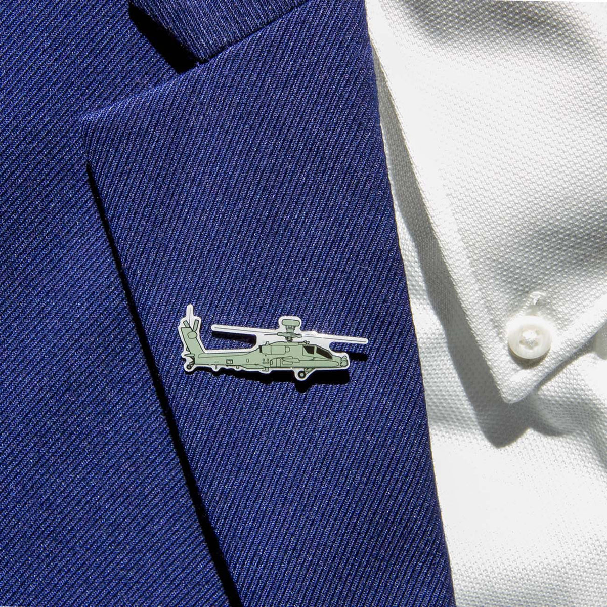 The Boeing Illustrated AH-64 Lapel Pin from The Boeing Store, featuring a silver-tone helicopter shape with an epoxy finish, adorns the blue textured suit lapel and complements the white shirt with visible buttons.
