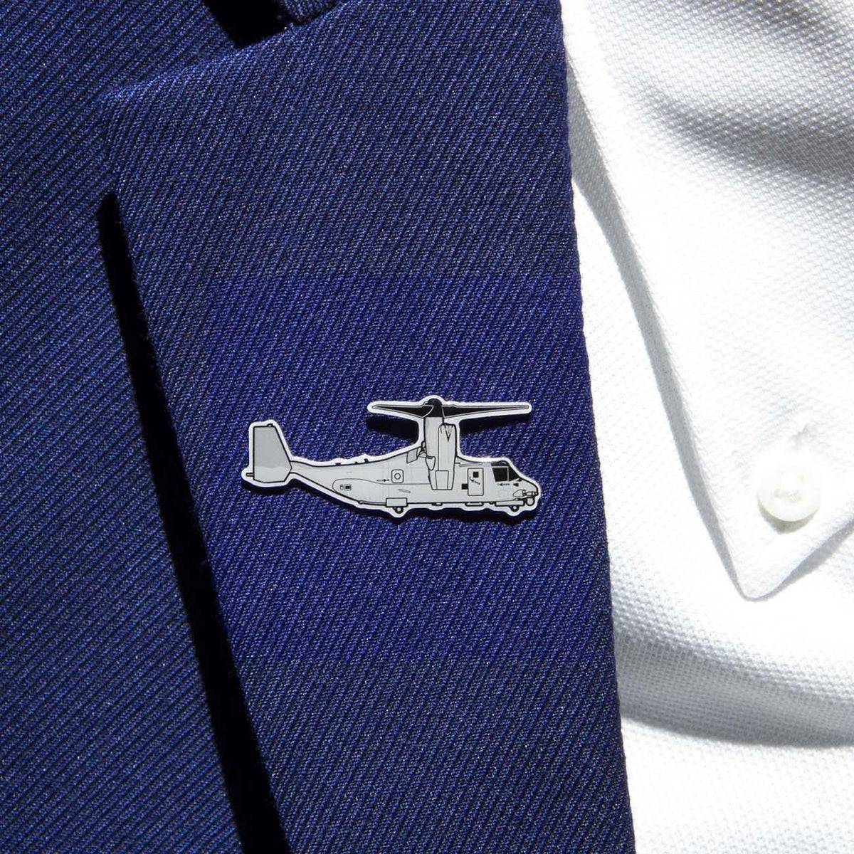 The Boeing Stores Boeing Illustrated V-22 Lapel Pin, in a silver tone with an aircraft outline and epoxy finish, adds elegance to the navy blue blazer lapel. It beautifully complements the white shirt beneath.