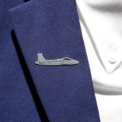 A close-up shows a person in a navy suit jacket adorned with The Boeing Stores silver-tone F-15 lapel pin. The gray fighter jet design enhances the sleek look, complemented by the visible buttons on the white shirt beneath.