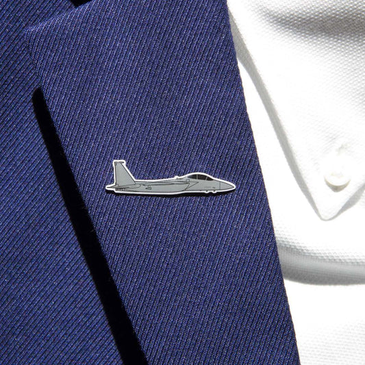 A close-up shows a person in a navy suit jacket adorned with The Boeing Stores silver-tone F-15 lapel pin. The gray fighter jet design enhances the sleek look, complemented by the visible buttons on the white shirt beneath.