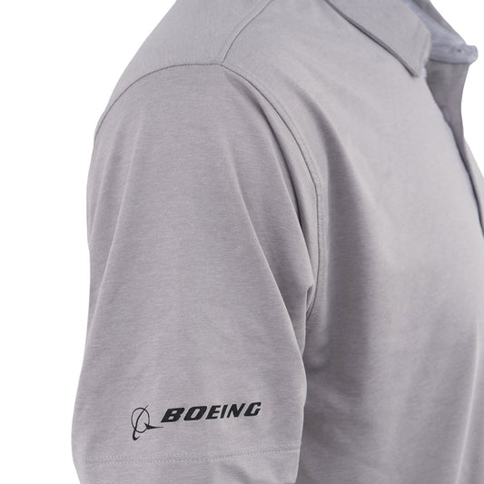 A close-up shows the upper torso of a person wearing the Boeing CH-47 Chinook Series Men’s Polo in light gray, featuring the black BOEING logo on the left sleeve and highlighting its moisture-wicking fabric for comfort.
