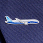 A silver-toned Boeing Illustrated 787 Lapel Pin from The Boeing Store, shaped like a Boeing airplane with an epoxy finish, adorns dark blue fabric. Its enhanced blue and white colors feature the Boeing logo prominently on the side.