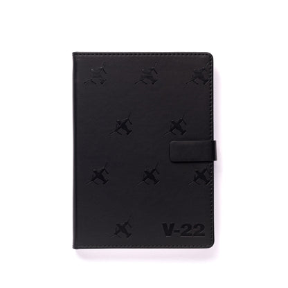 The Boeing Stores Boeing V-22 Osprey Notebook features a black PU hardcover with snap closure, stamped with small V-22 Osprey patterns and V-22 at the bottom right on a white background—ideal for any Boeing notebook fan.