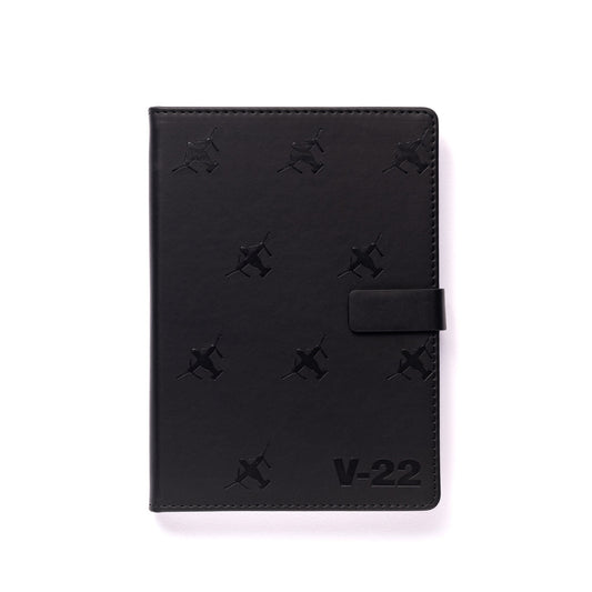The Boeing Stores Boeing V-22 Osprey Notebook features a black PU hardcover with snap closure, stamped with small V-22 Osprey patterns and V-22 at the bottom right on a white background—ideal for any Boeing notebook fan.