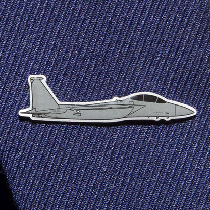 The Boeing Store presents the Boeing Illustrated F-15 Lapel Pin, a sleek gray fighter jet pin with black outlines and an epoxy finish. Its set against blue textured fabric, perfect for suits or ties.